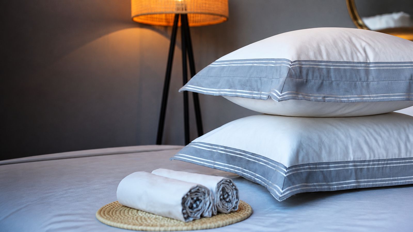 Grey Melchiah bedding finished with a charcoal striped border, styled with a rattan lamp
